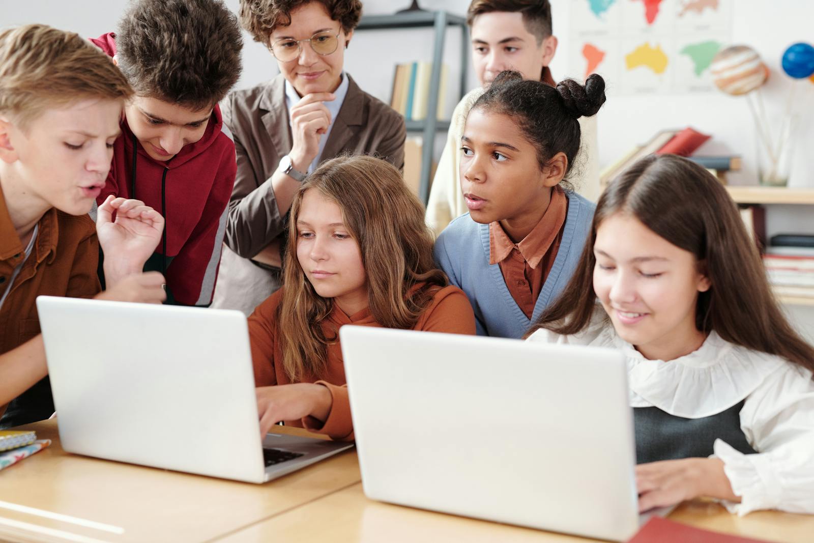 Teenage students actively collaborate on laptops in an educational environment with guidance from a teacher.