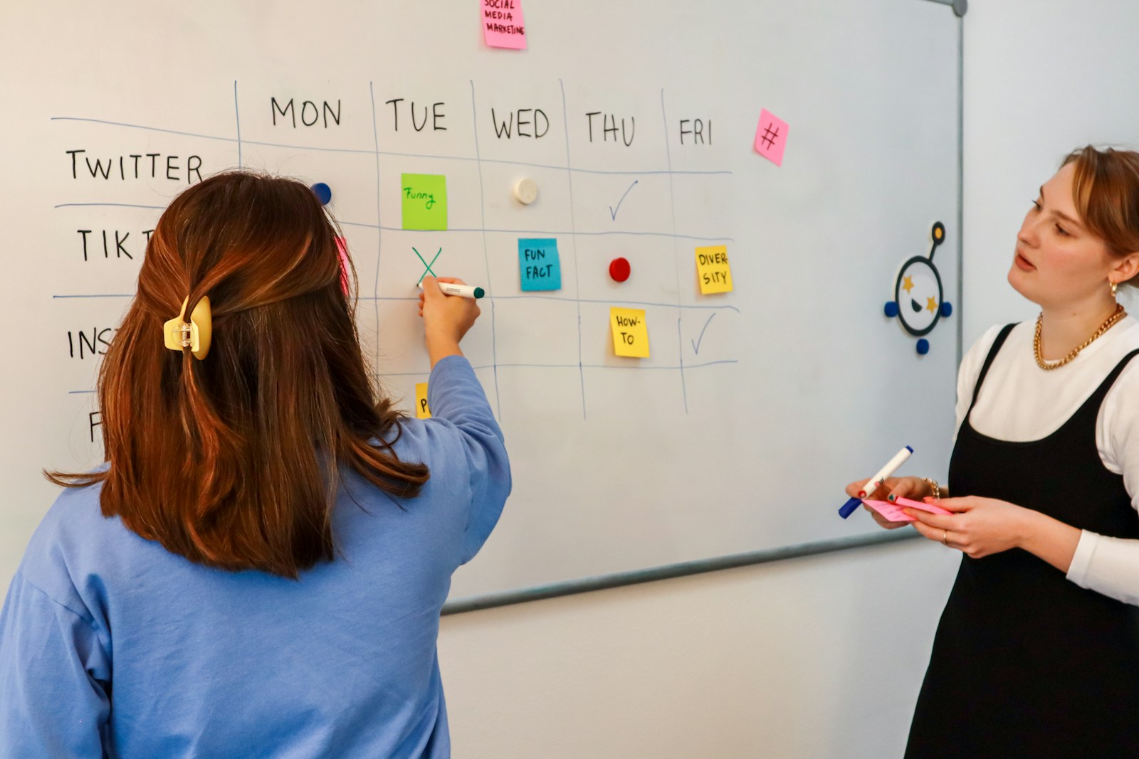 two women writing on a white board with sticky notes